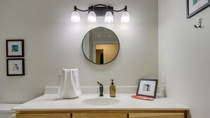 A bathroom with a round mirror, a white sink, wooden cabinets, a towel, a soap dispenser, and a framed picture. - Wadena Vacation Rental ~ 1 Mi to Downtown! (Wadena)