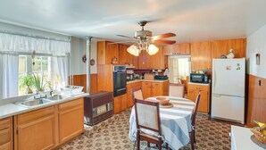 A kitchen with wooden cabinets, a dining table with chairs, a ceiling fan, and a refrigerator.