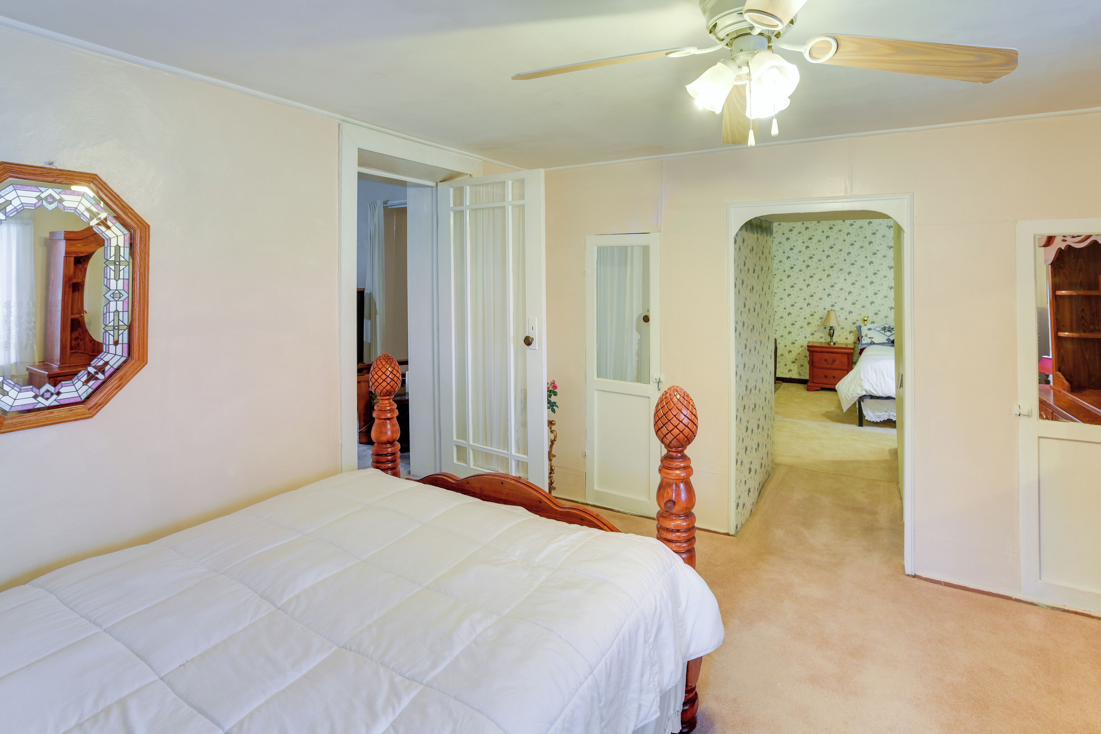 Une chambre à coucher avec un lit, un ventilateur de plafond et une porte donnant sur une autre pièce.