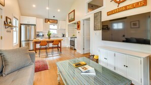 Una cocina moderna con armarios blancos, un refrigerador de acero inoxidable y un comedor con mesa y sillas de madera.