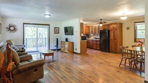 A spacious living area with a sofa, dining table, and kitchen with wooden cabinets and appliances. - Riverfront Covington Cabin w/ Deck & Fire Pit! (Covington)