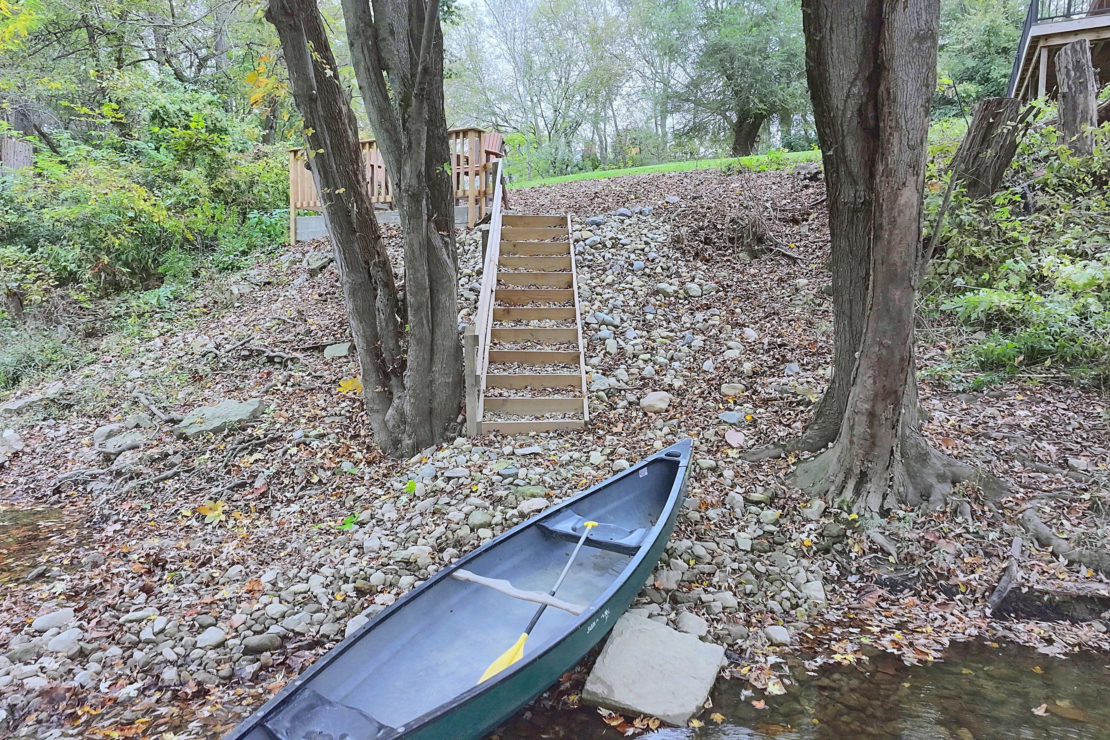A canoe on a pebble-strewn shore with a wooden staircase leading up to a wooden structure.