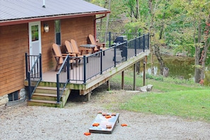 A wooden cabin with a deck, outdoor seating, and a view of a lake.
