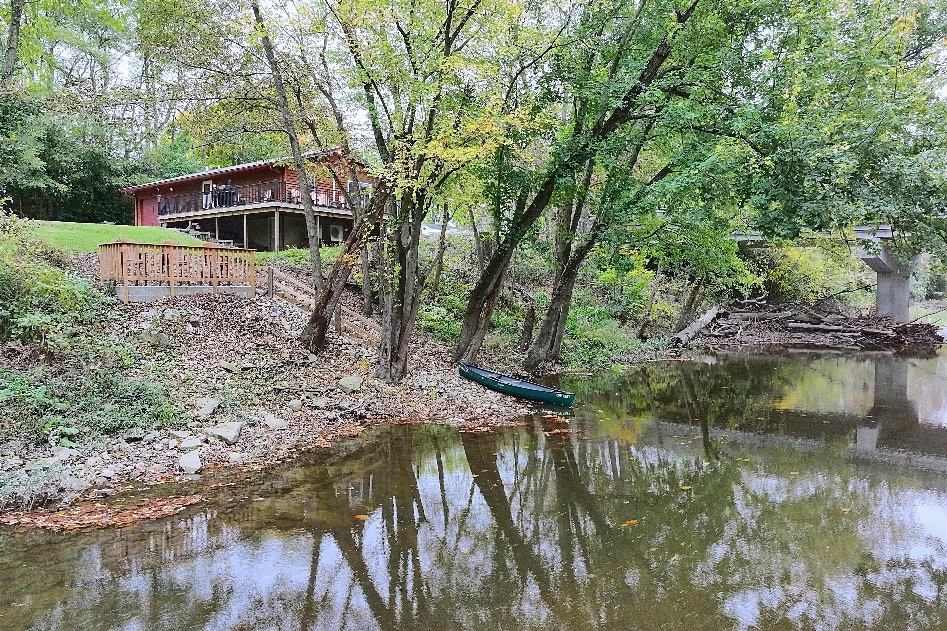 Una cabaña junto al lago con un balcón y asientos al aire libre, rodeada de árboles y una masa de agua tranquila.