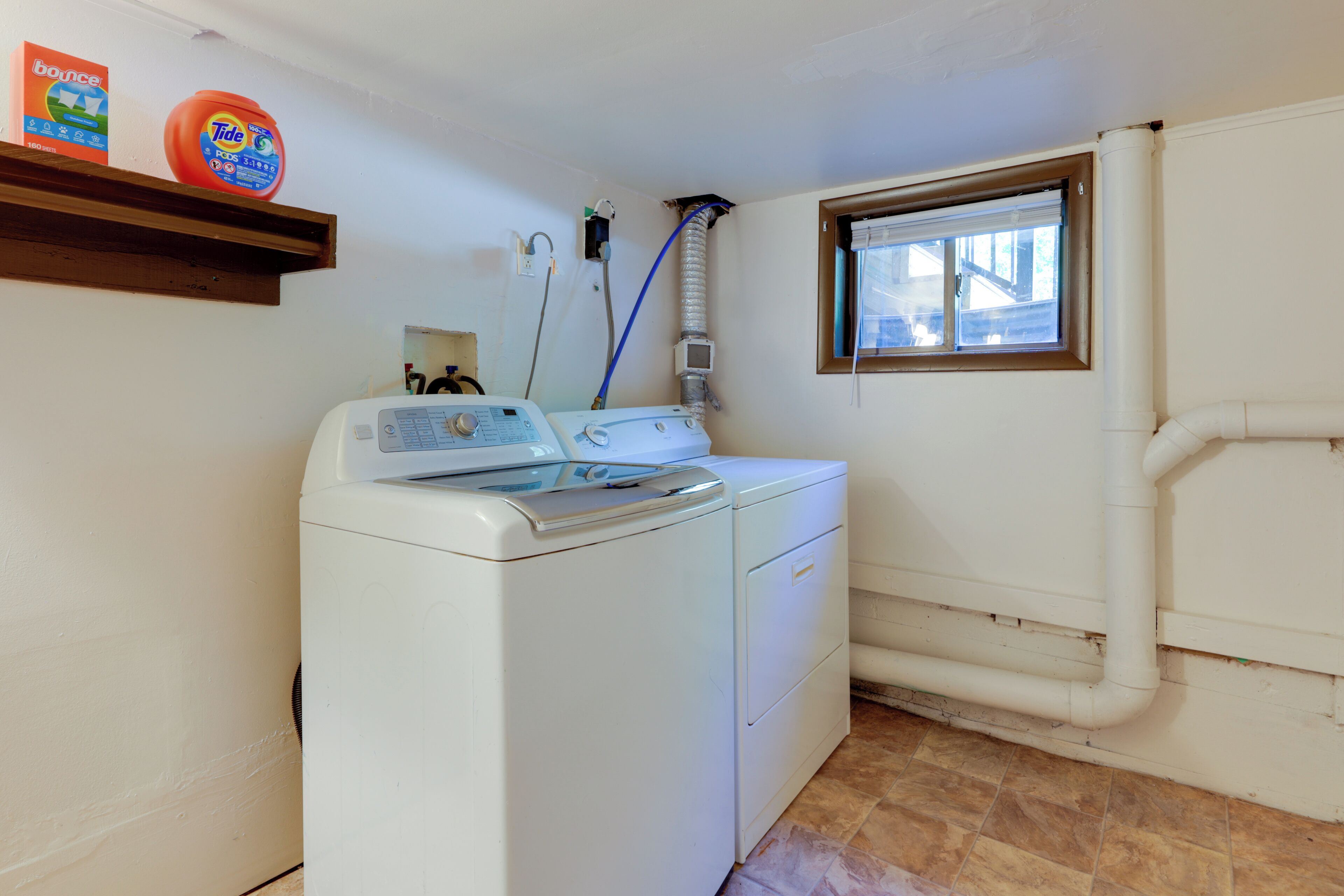 A laundry area with a front-loading washer and dryer, a window, and a shelf with laundry detergent.