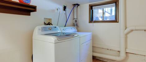 A laundry area with a front-loading washer and dryer, a window, and a shelf with laundry detergent.