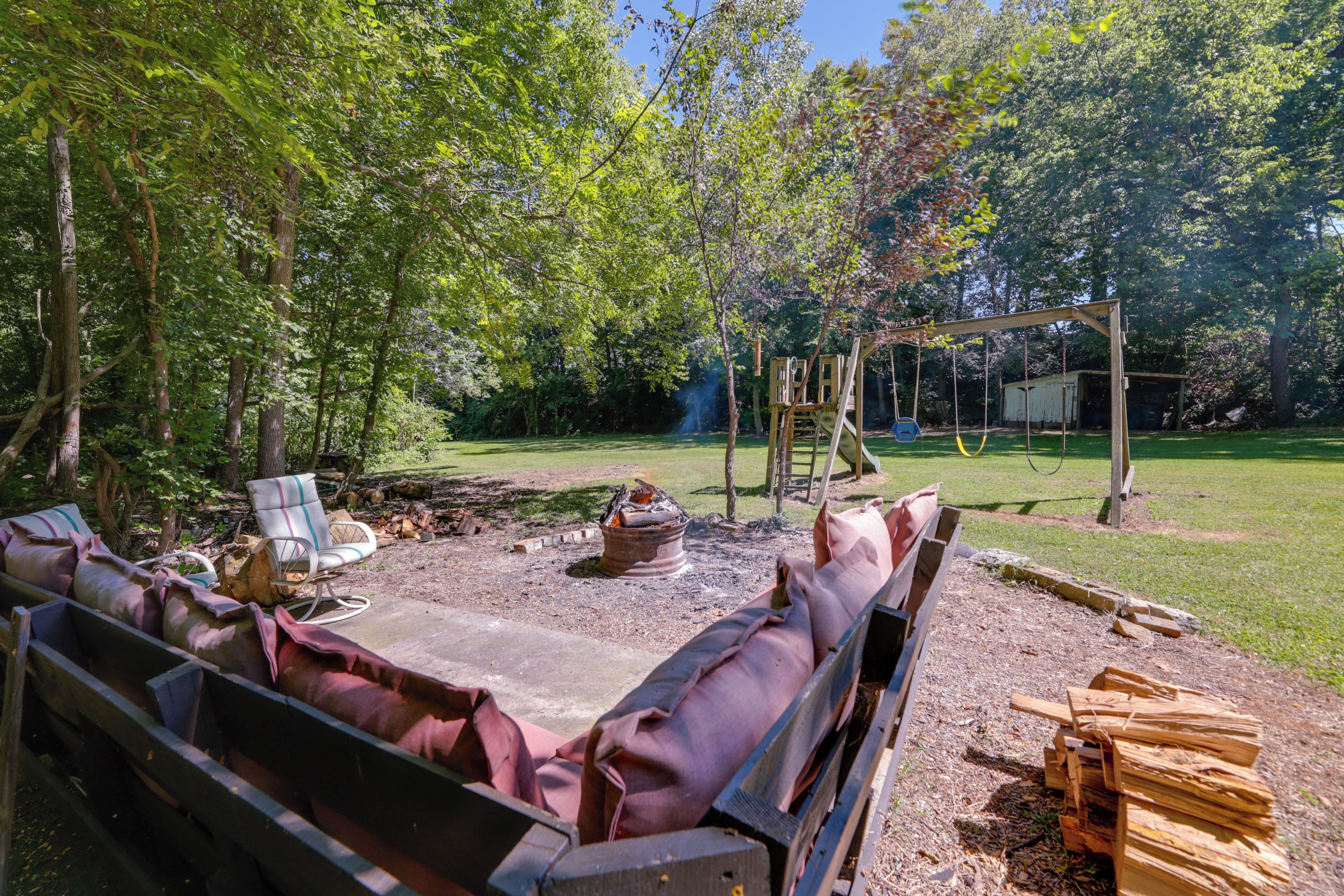 A backyard with a fire pit, wooden seating, and a swing set.
