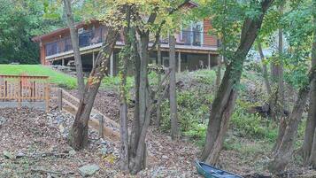 A cabin with a deck overlooking a body of water, surrounded by trees and a wooden fence.