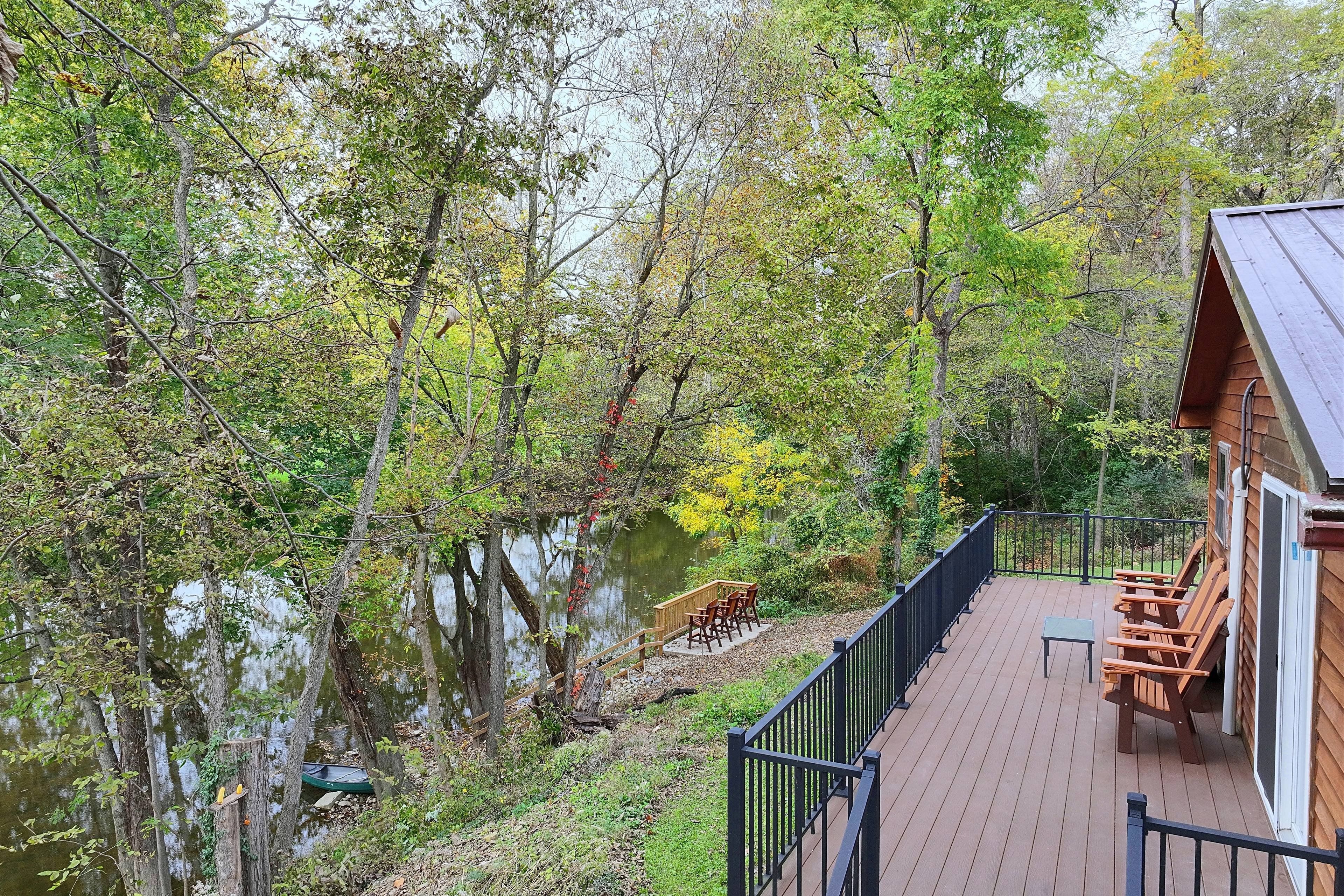 A wooden deck with outdoor furniture overlooking a body of water and dense foliage.