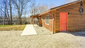 A wooden cabin with a red door, a porch, and a gravel driveway. - Riverfront Covington Cabin w/ Deck & Fire Pit! (Covington)
