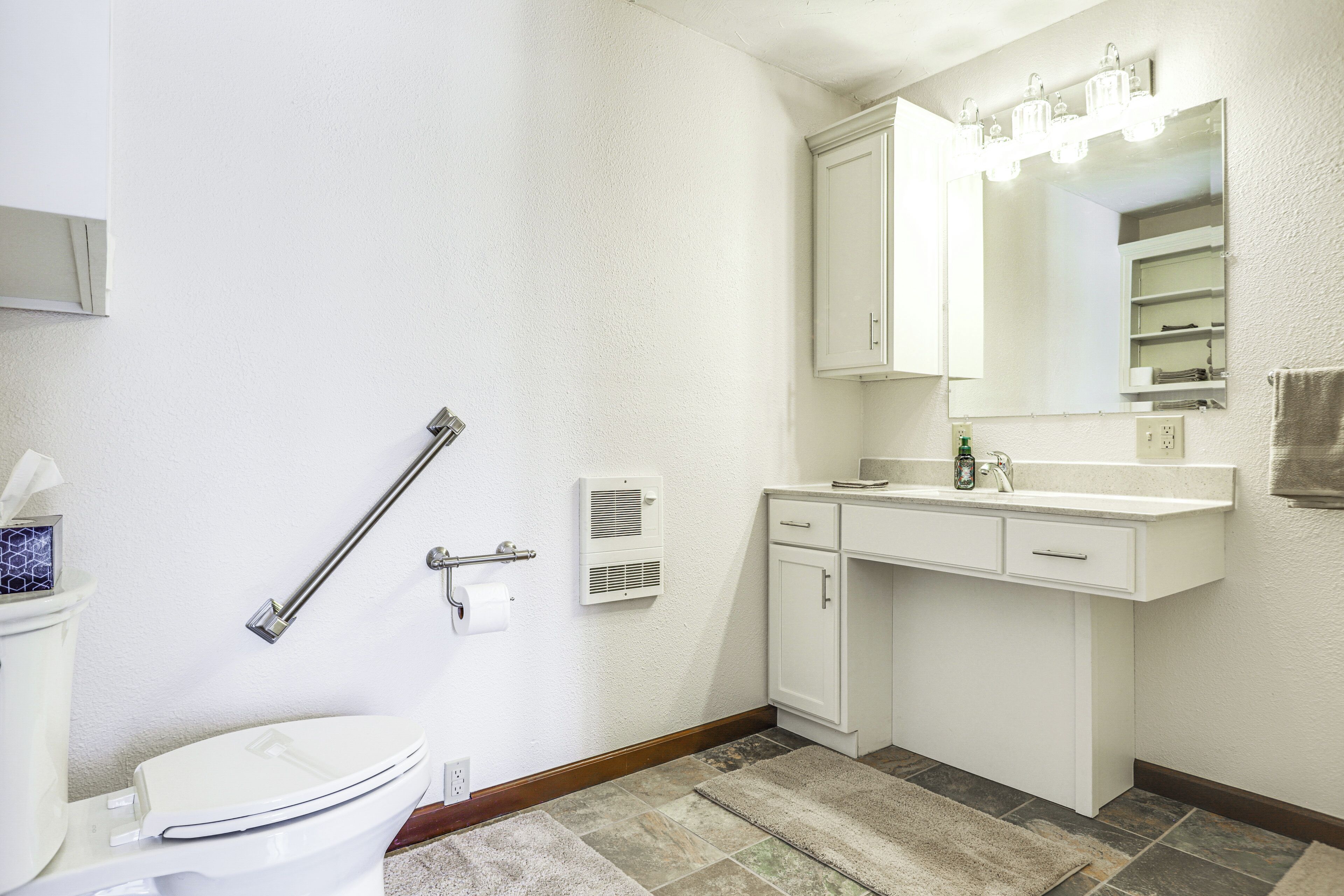 A bathroom with a toilet, a sink with a mirror, and a handrail.