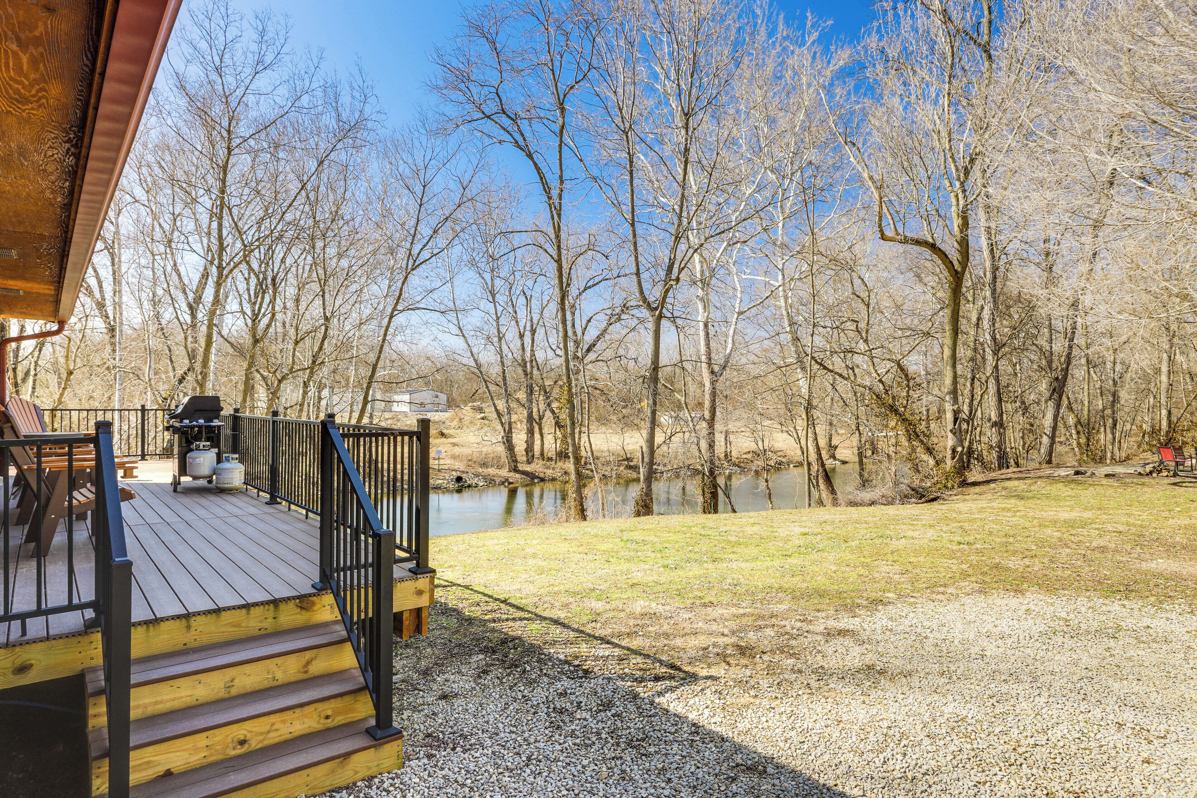 A wooden deck with a barbecue grill, a bench, and a view of a river and trees.