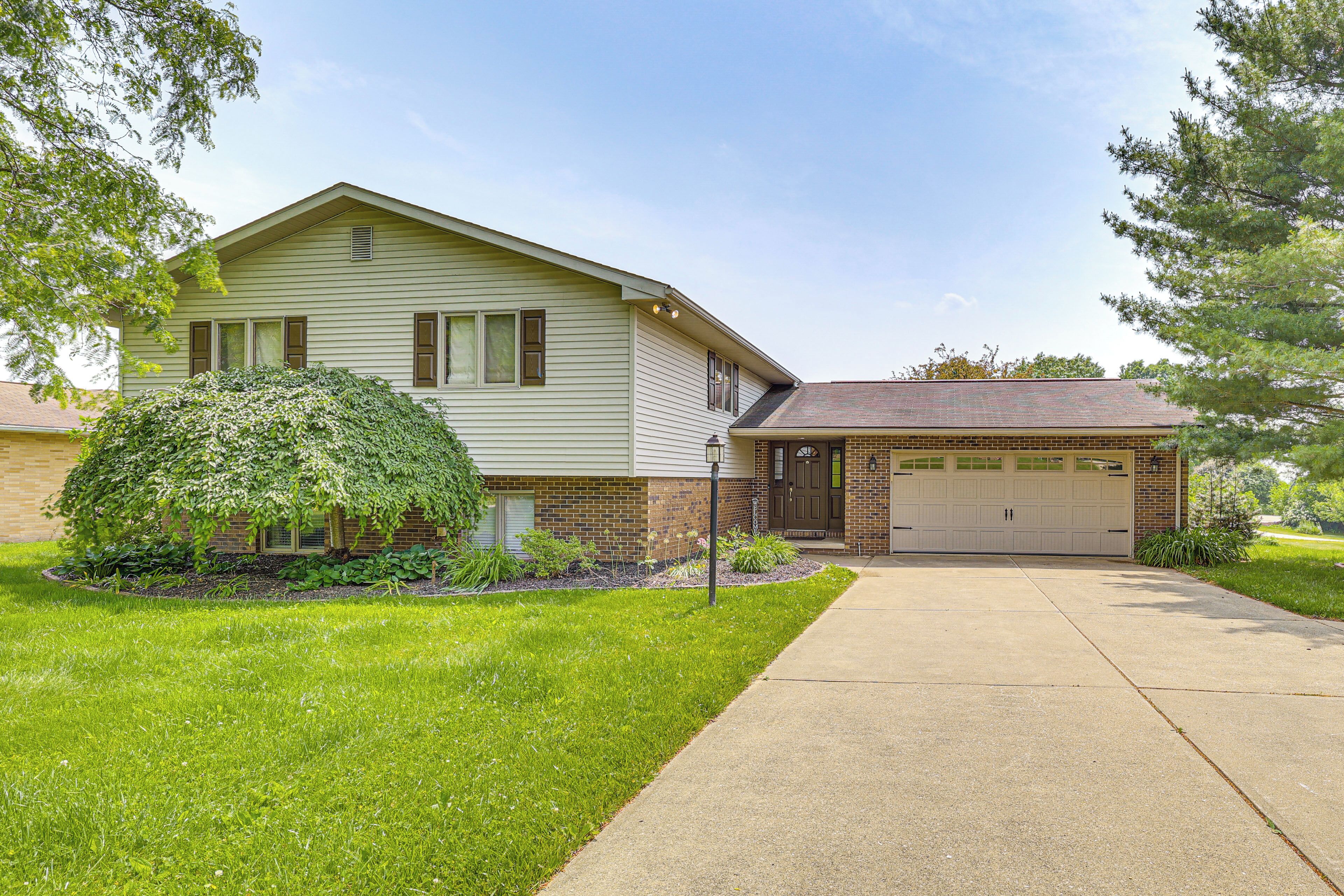 A two-story house with a garage, a well-maintained lawn, and a large tree in front.