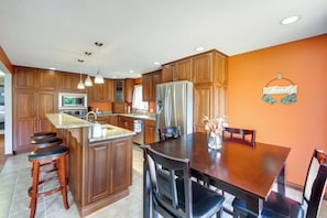A kitchen with wooden cabinets, a stainless steel refrigerator, and a dining area with a table and chairs.