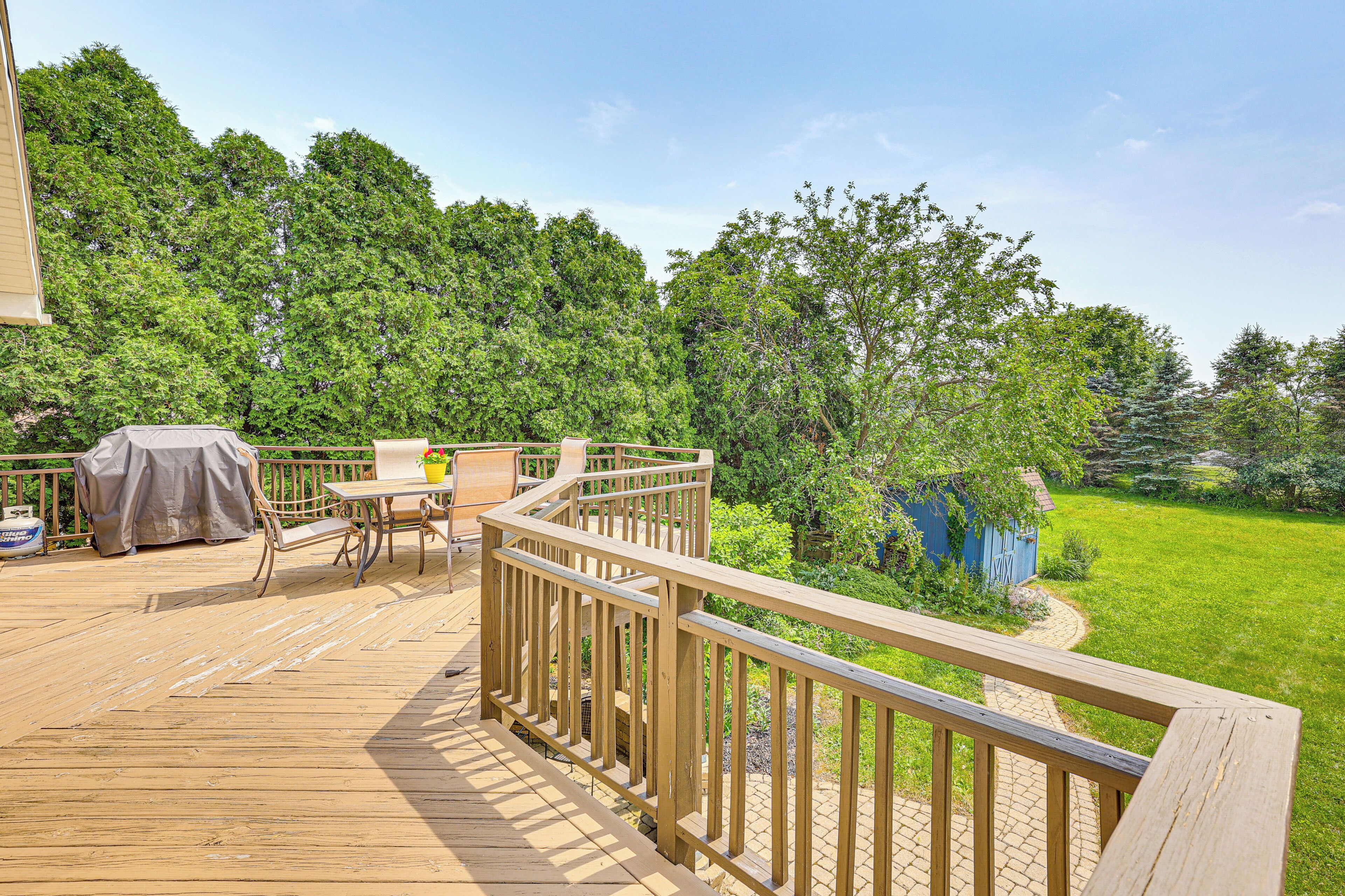 Eine Holzterrasse mit Gartenmöbeln, einem Grill und Blick auf einen üppigen Garten und Bäume.