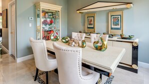 A dining area with a white table, two white chairs, a glass cabinet with decorative items, and a kitchen counter with a white cabinet. - Centrally Located Family Home w/ Pool (Harleysville)