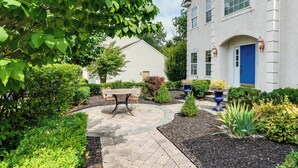 A well-maintained garden with a patio table and chairs, surrounded by various shrubs and plants. - Centrally Located Family Home w/ Pool (Harleysville)