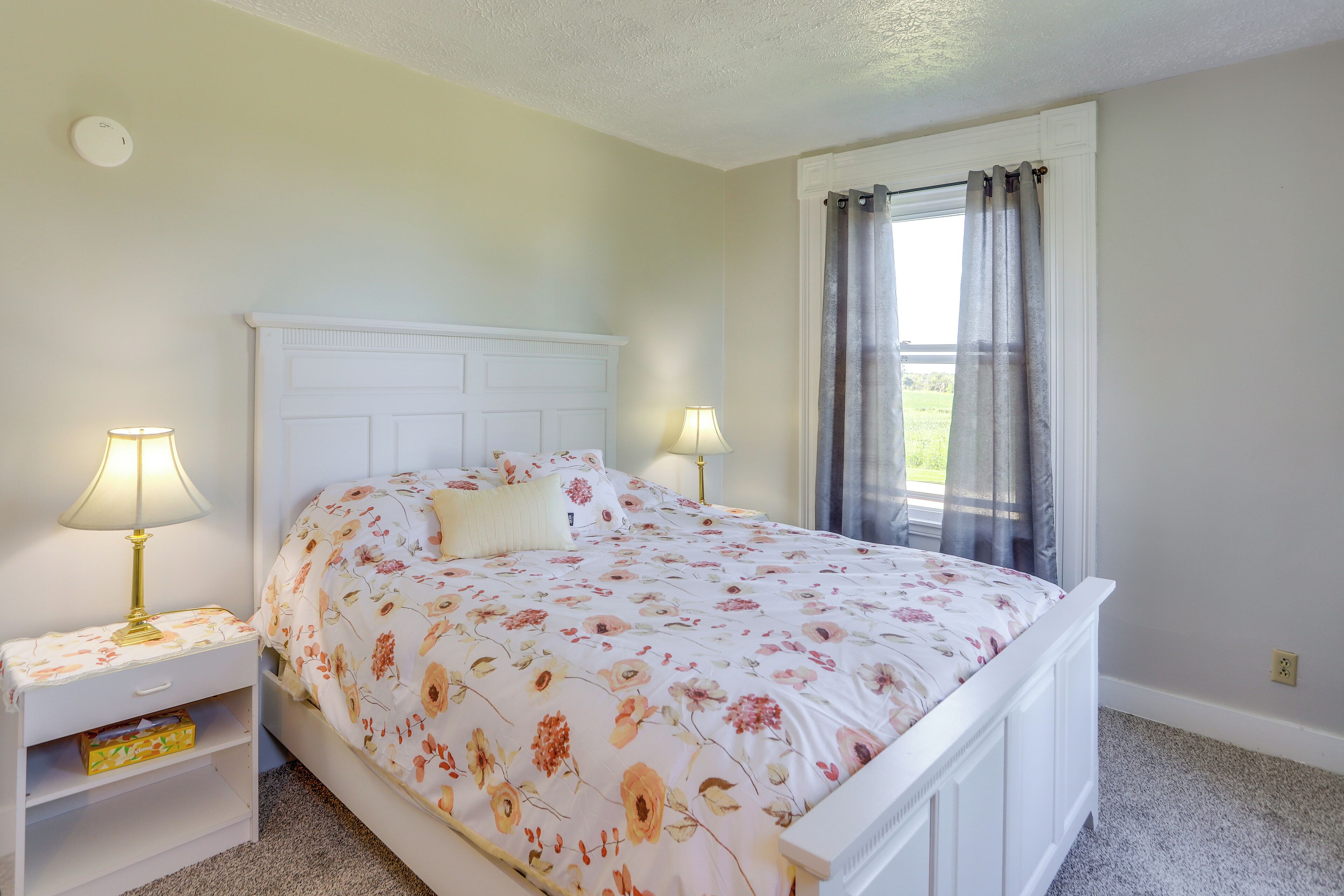 A neatly made bed with floral bedding, two bedside lamps, and a nightstand with a drawer.