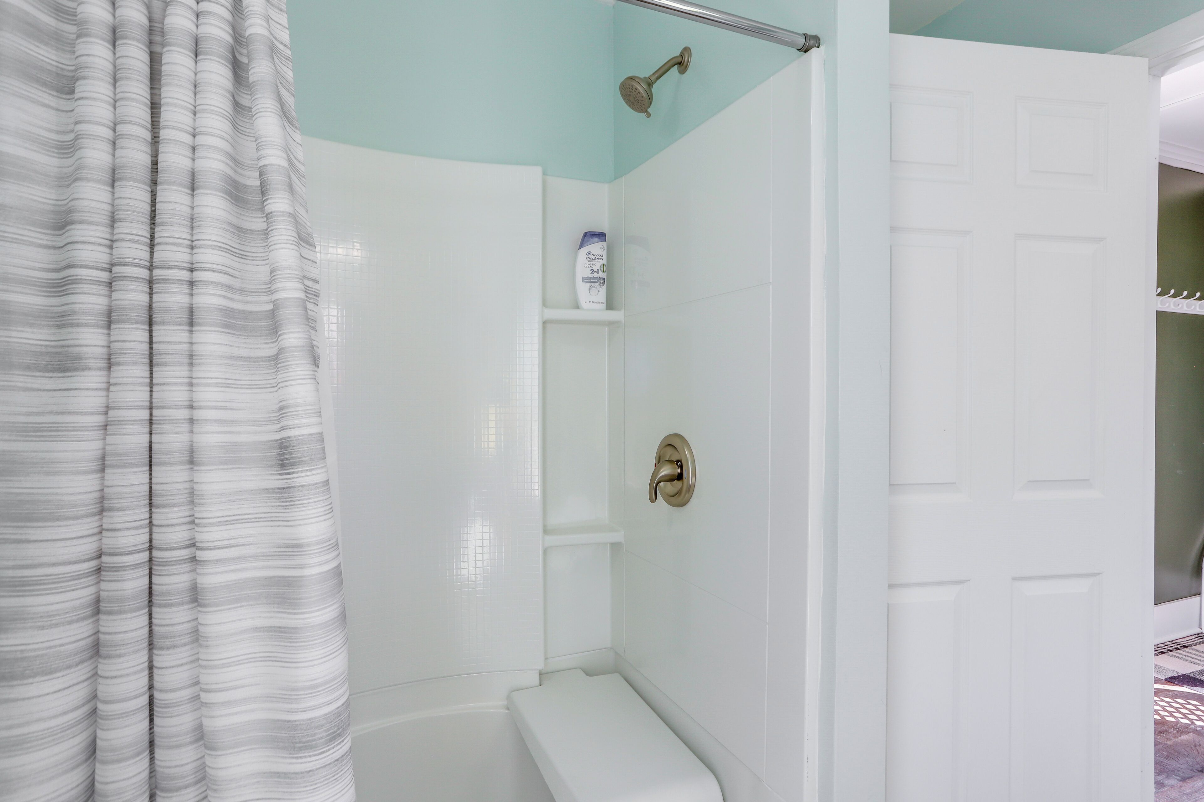 A bathroom with a shower, toilet, and a door leading to another room.