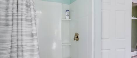 A bathroom with a shower, toilet, and a door leading to another room.