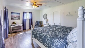Una camera da letto con un letto, una ventola a soffitto, una finestra con tende, un comodino, una sedia e uno specchio fissato alla parete.