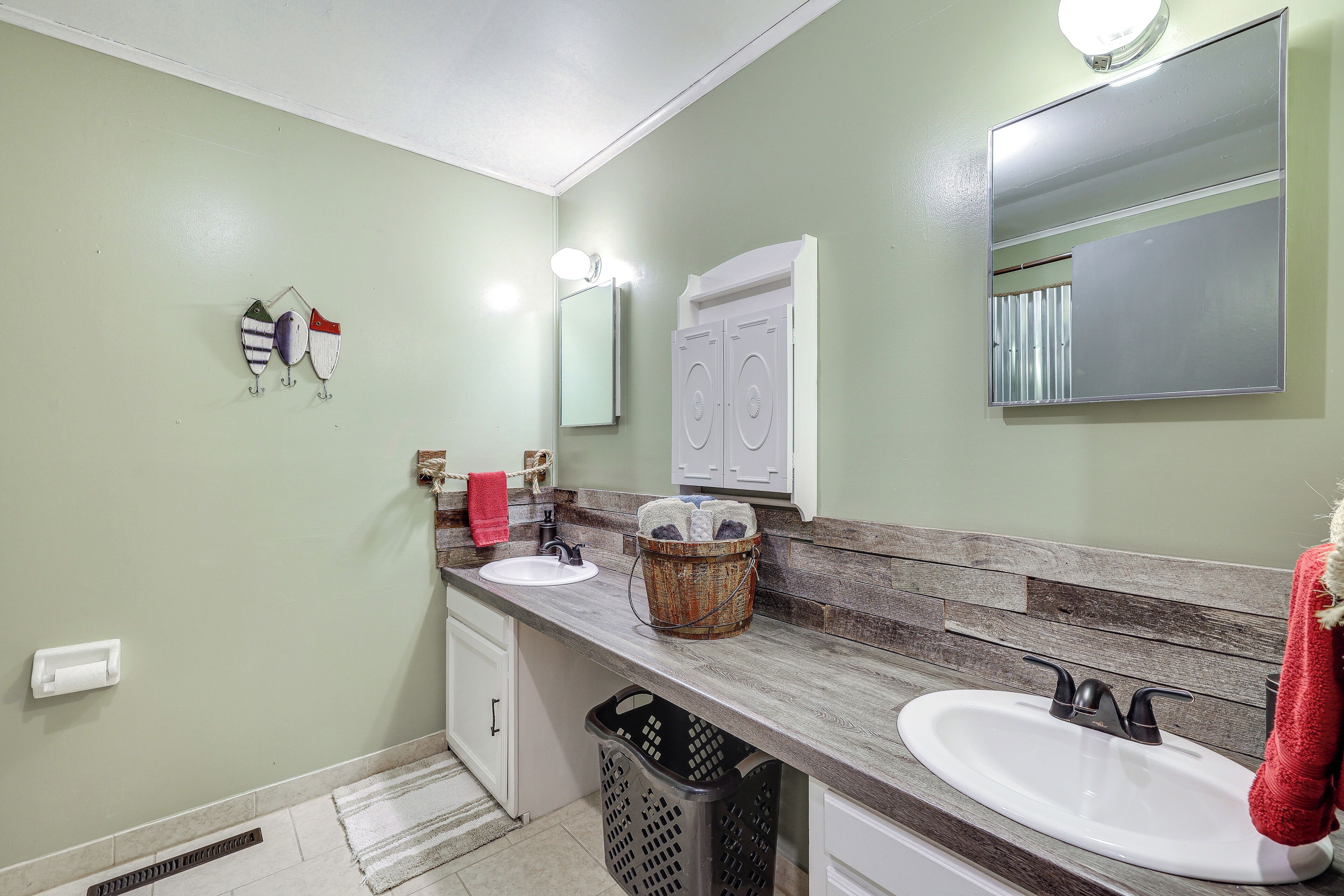 A bathroom with two sinks, a mirror, and a laundry basket on the counter.