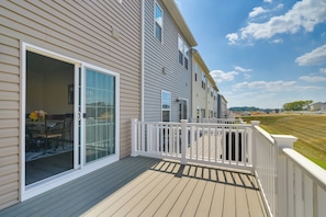A residential deck with a sliding glass door leading to a dining area, a white railing, and a clear view of a grassy field and distant buildings. - Spacious Hedgesville Retreat ~ 5 Mi to Golf Course (Hedgesville)