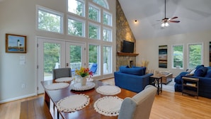 A spacious living room with a large wooden dining table, blue sofas, and a stone fireplace. - Waterfront Hartfield Vacation Rental w/ Dock! (Hartfield)