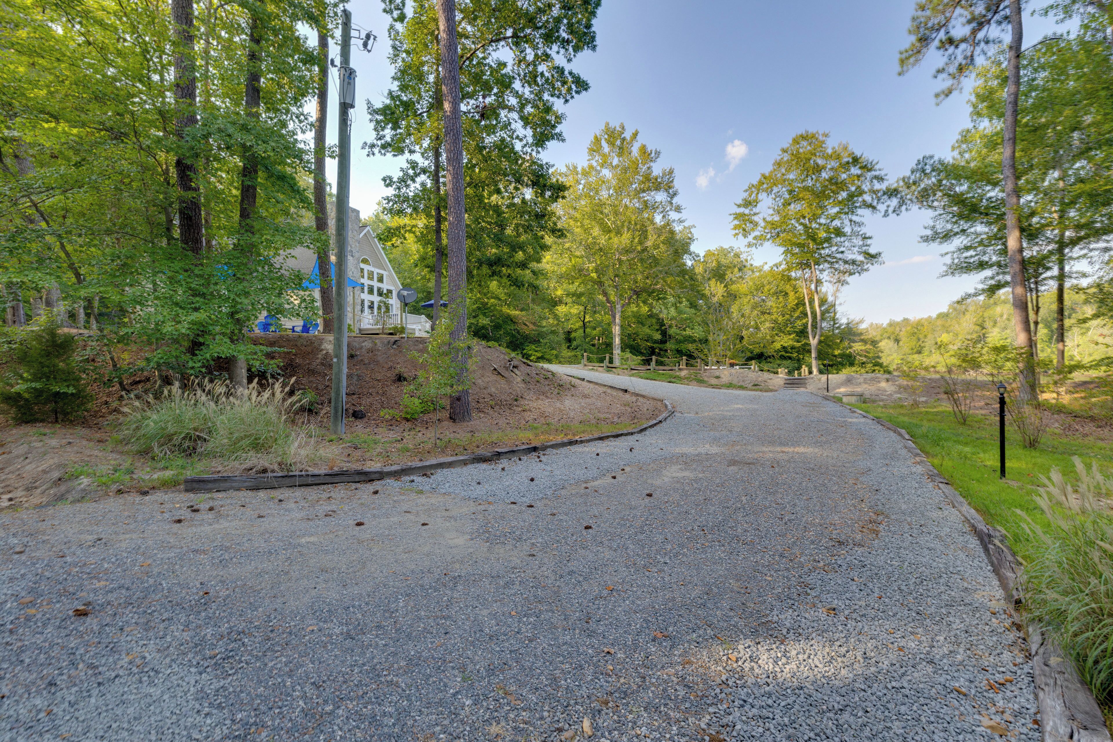 A gravel driveway curving through a wooded area with a house on the left.