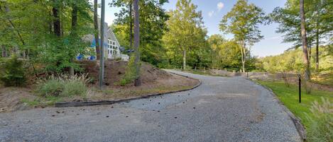 A gravel driveway curving through a wooded area with a house on the left.