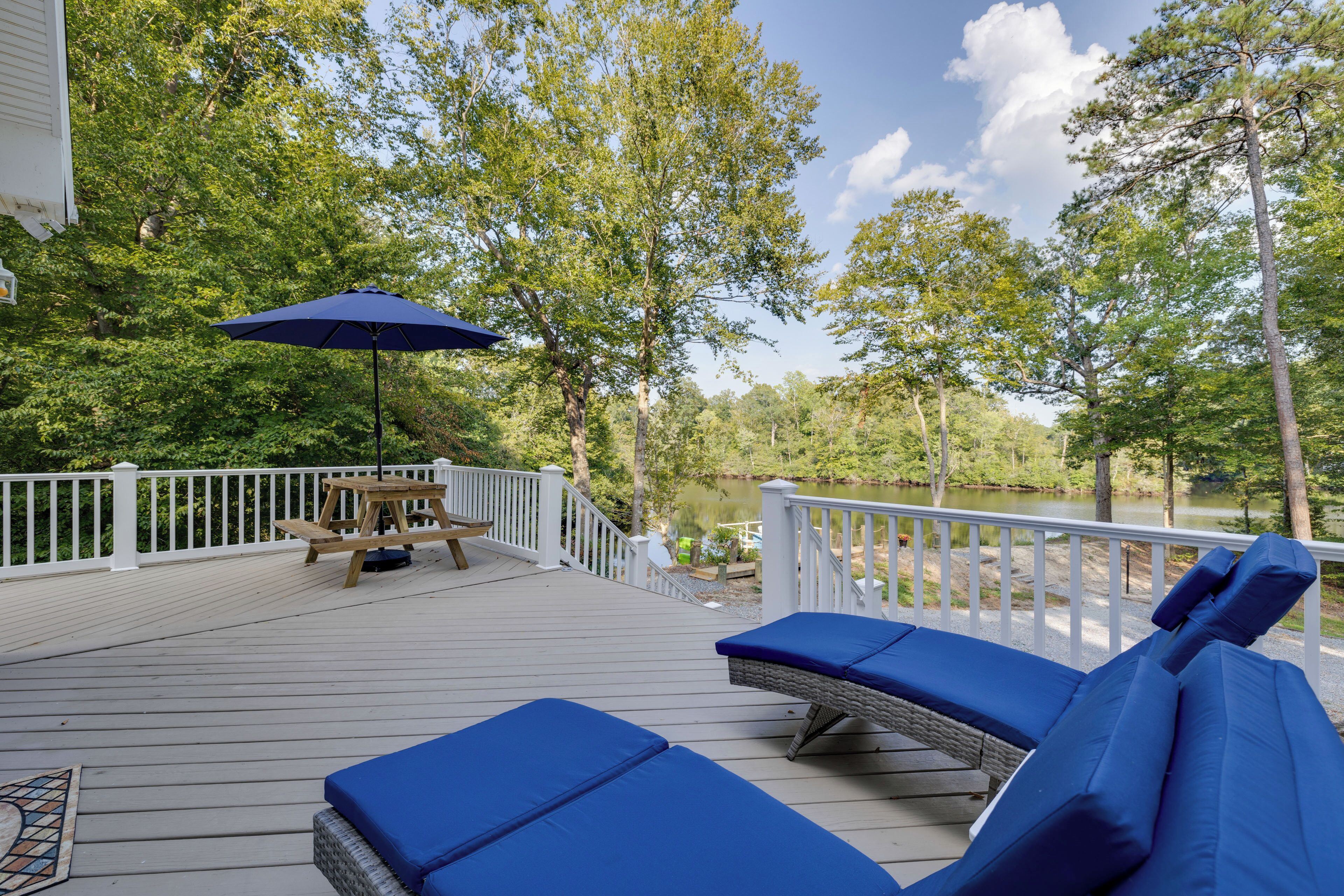 Une terrasse en bois avec des chaises longues bleues et une table de pique-nique, donnant sur un lac.