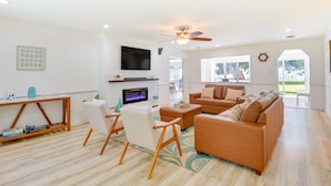 A spacious living room with a large sofa, a TV mounted on the wall, and a ceiling fan. - Sun-dappled Waterfront Home on Potomac River! (Scotland)