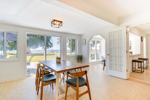 A spacious dining area with a wooden table and chairs, large windows offering a view of the outdoors, and a white door leading to another room. - Sun-dappled Waterfront Home on Potomac River! (Scotland)