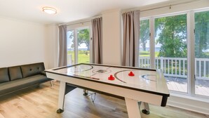 A room with a foosball table, a sofa, and large windows with curtains. - Sun-dappled Waterfront Home on Potomac River! (Scotland)