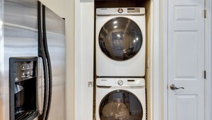 Une petite buanderie équipée de deux machines à laver et deux sèche-linge superposés, d’un distributeur d’eau et d’une porte.