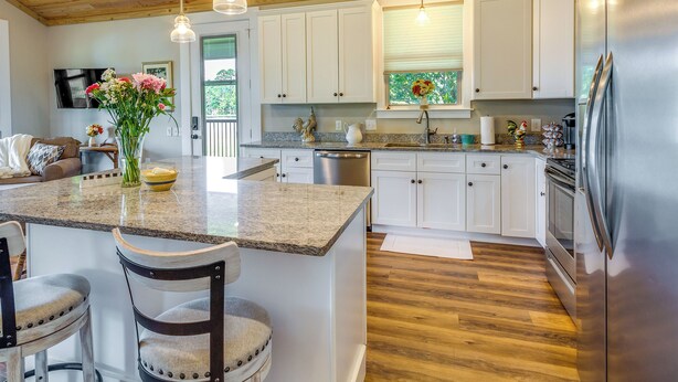 A modern kitchen with white cabinets, a granite countertop, stainless steel appliances, and wooden flooring. - Escape to Nature: Lakefront Jay Cottage w/ Views! (Jay)