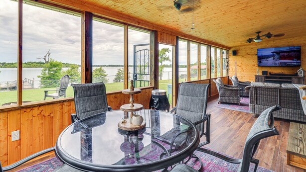 Una habitación amplia con una gran mesa de vidrio y sillas, paredes de madera y vista a un lago.