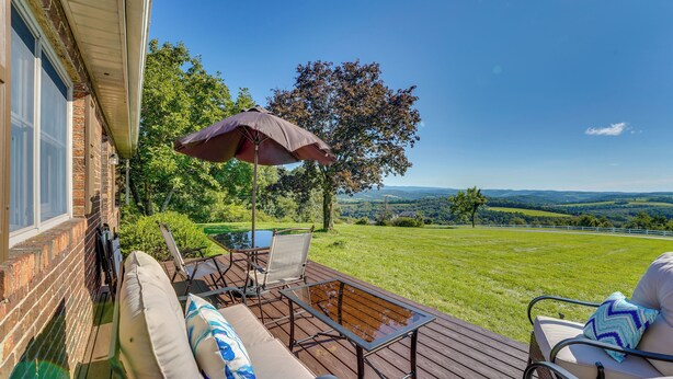 A deck with outdoor furniture, a table, and an umbrella, overlooking a grassy landscape with trees and hills. - Muncy Vacation Rental w/ Deck & Views (Muncy)