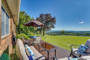 Une terrasse dotée de mobilier d’extérieur, d’une table et d’un parasol, offrant une vue sur un paysage verdoyant avec des arbres et des collines.