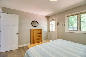 Relax in this serene bedroom with a comfortable bed, dresser, and mirror, offering a peaceful view of the surrounding greenery.