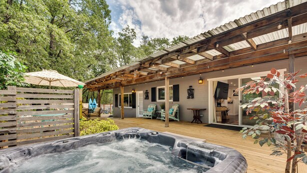 A hot tub in a wooden deck area with a pergola overhead, surrounded by greenery and a covered patio with outdoor seating. - Modern Meadow Vista Vacation Home w/ Spacious Deck (Meadow Vista)