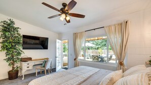 A bedroom with a bed, a desk, a chair, a ceiling fan, a TV, a window with curtains, and a potted plant. - Modern Meadow Vista Vacation Home w/ Spacious Deck (Meadow Vista)
