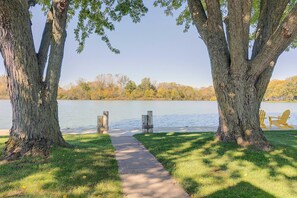 Un sentier qui mène à un lac, bordé de chaque côté d’arbres et d’une rangée de fauteuils Adirondack.
