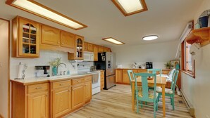 Een keuken met houten kastjes, een wit aanrecht, een eettafel met stoelen en een koelkast.