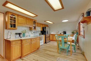 Een keuken met houten kastjes, een wit aanrecht, een eettafel met stoelen en een koelkast.