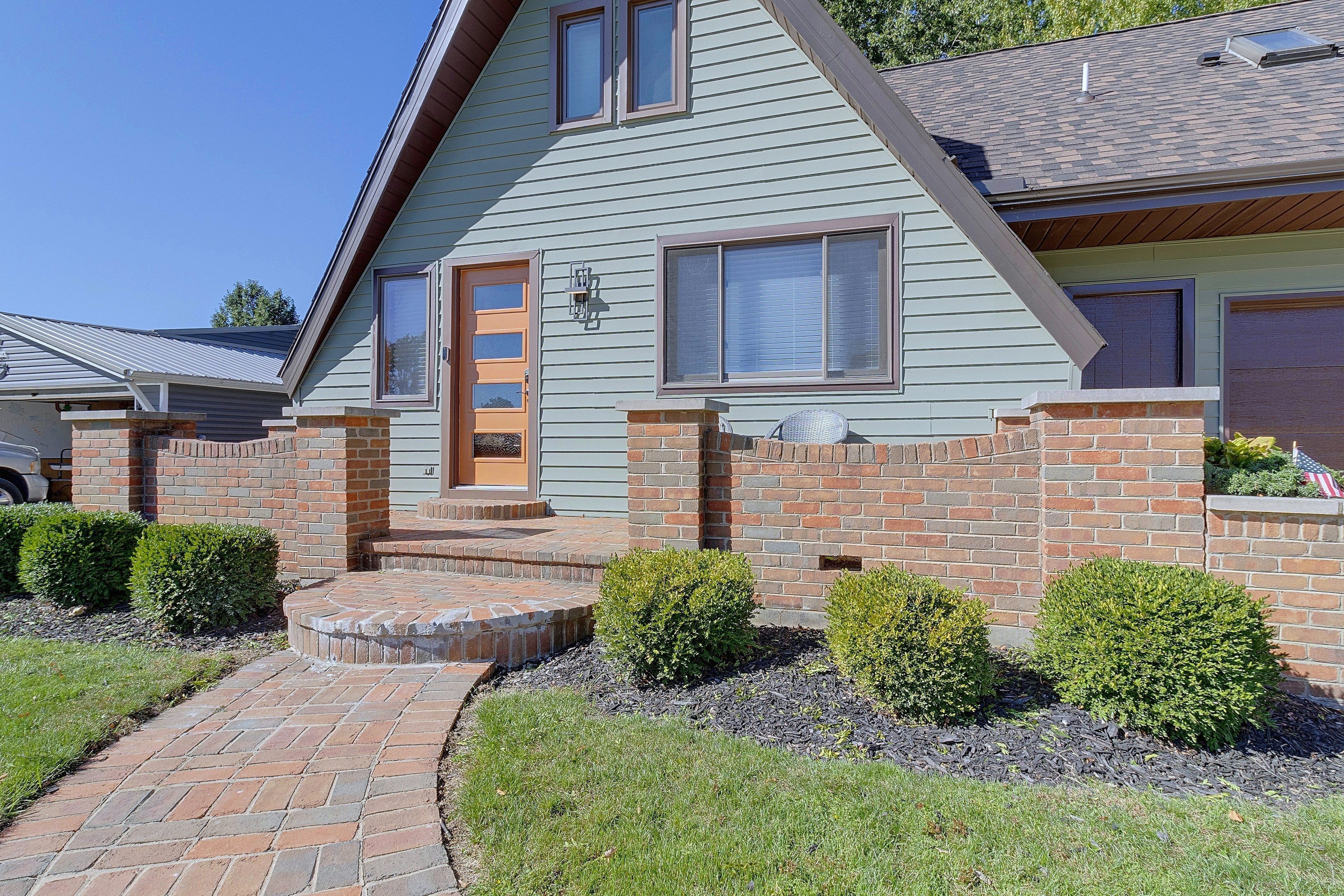 A two-story house with a brick exterior, a front porch, and a small garden area.