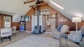 A loft-style living room with a high ceiling, a fireplace, a staircase, and a cozy seating area.