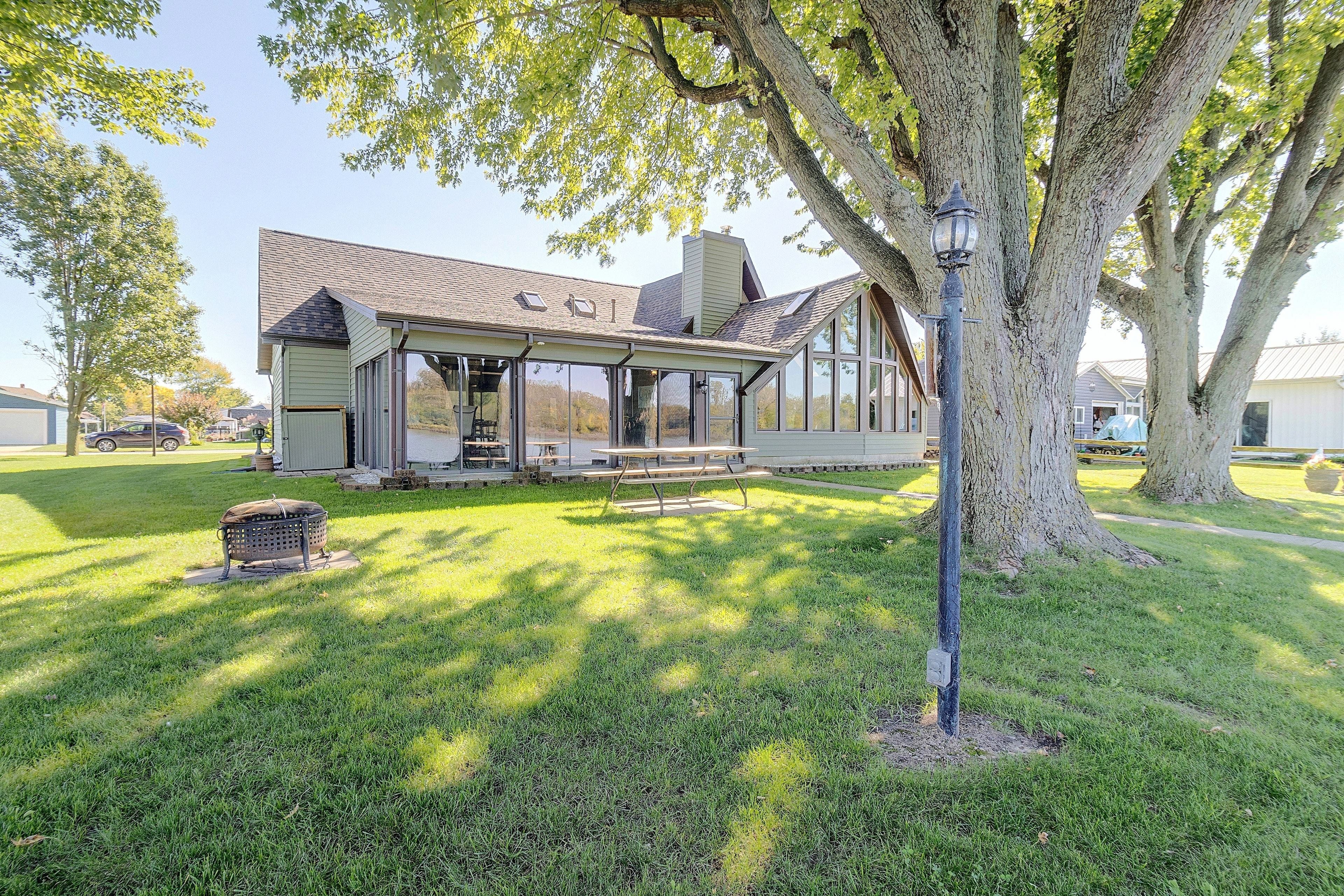A house with a covered patio, a lawn, and a large tree.