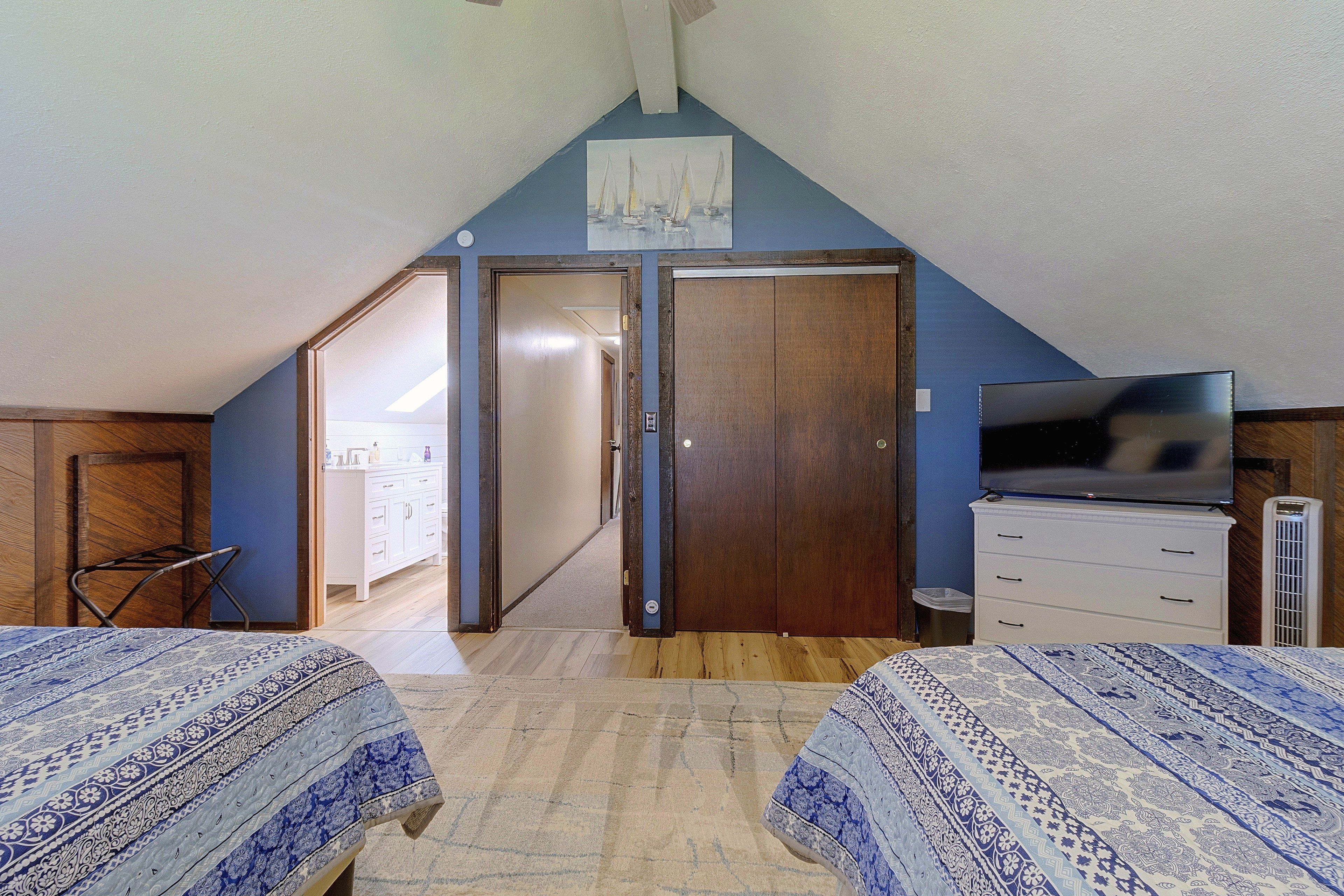 A bedroom with two beds, a TV, a wardrobe, and a door leading to a bathroom.