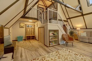 A spacious loft with a high ceiling, exposed wooden beams, a central staircase, and a cozy seating area with a leather armchair and a sofa. - Lakefront St Marys Getaway w/ Boat Dock + Fire Pit (St. Marys)